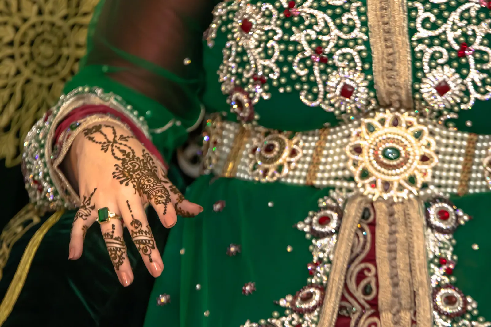 Henna-decorated hands on an embroidered green caftan